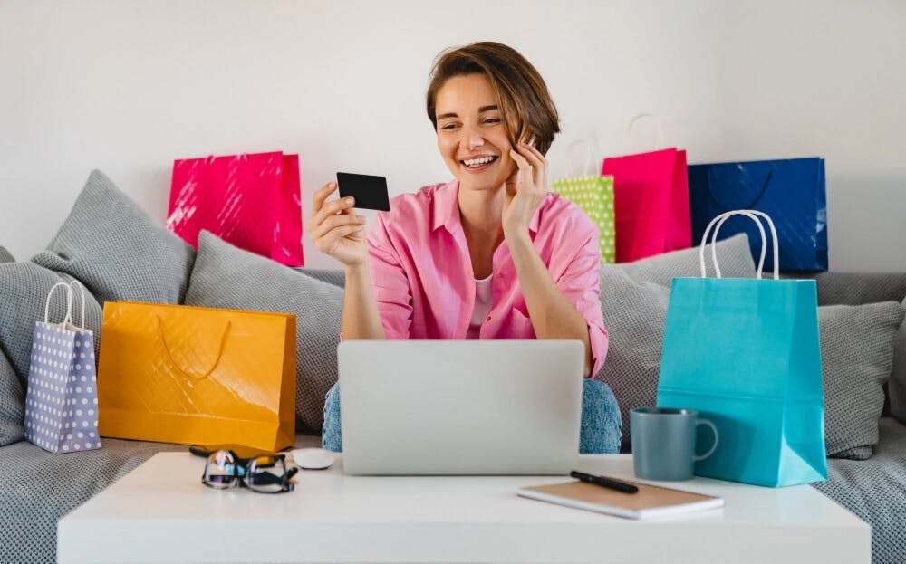 Zadowolona młoda kobieta w różowej bluzce robiąca zakupy przez Internet
