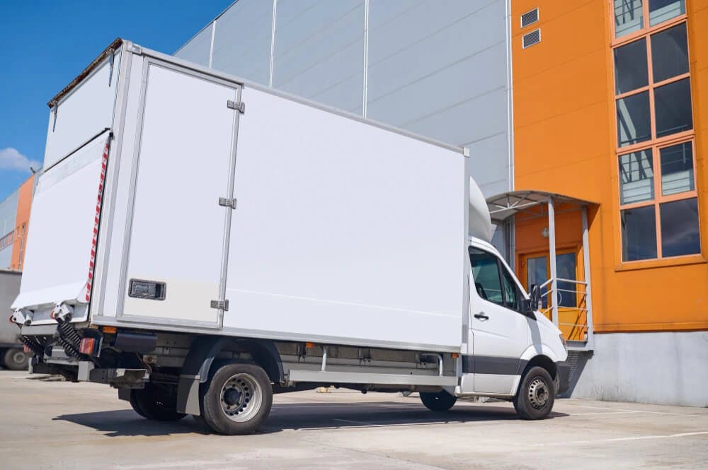 Transport małym pojazdem ciężarowym – biała furgonetka zaparkowana pod sklepem
