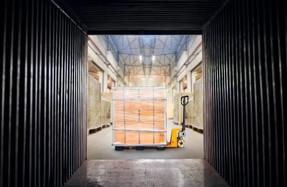 Transport jednostki logistycznej – wózek widłowy z paletą, na której znajdują się równo ułożone i zafoliowane kartony.